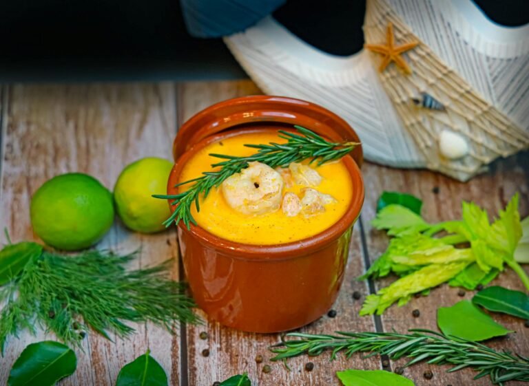 A bowl of soup with shrimp, herbs and lime